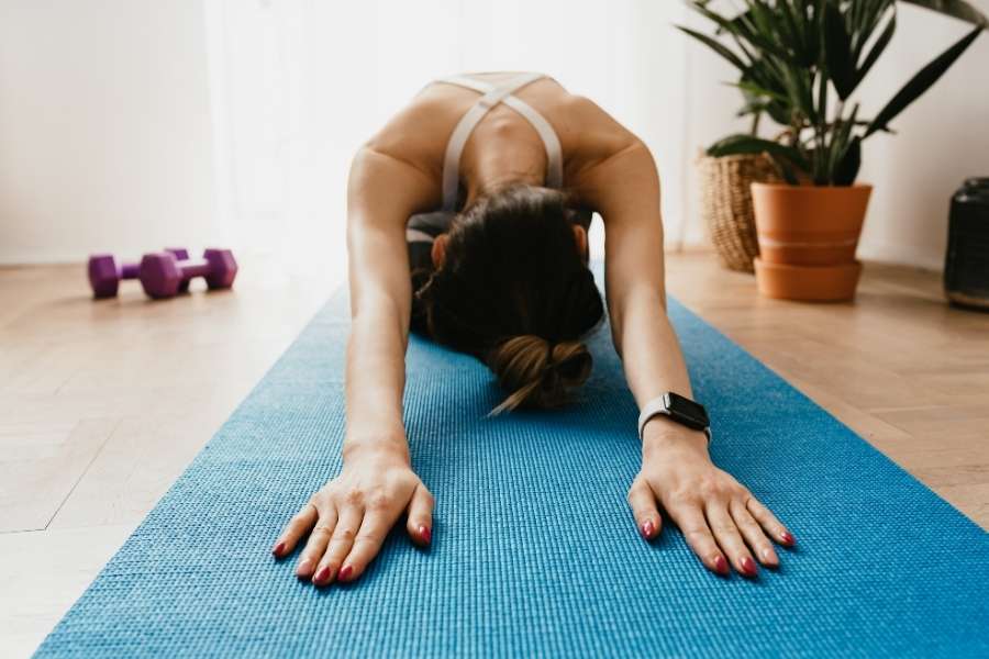 Une personne pratique des étirements sur un tapis, hésitant entre le yoga ou pilates pour sa séance.