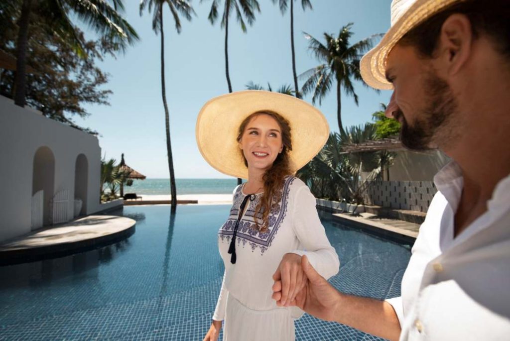 Couple en tenue estivale au bord d'une piscine face à la mer pour planifier sa lune de miel juste apres le mariage.