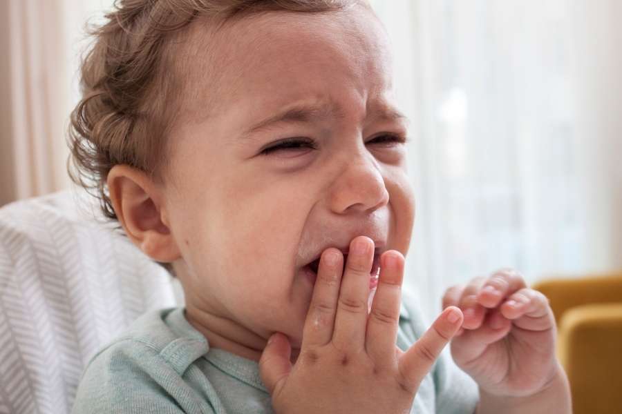 Un bébé en pleurs porte sa main à sa bouche, montrant une douleur due aux poussées dentaires.